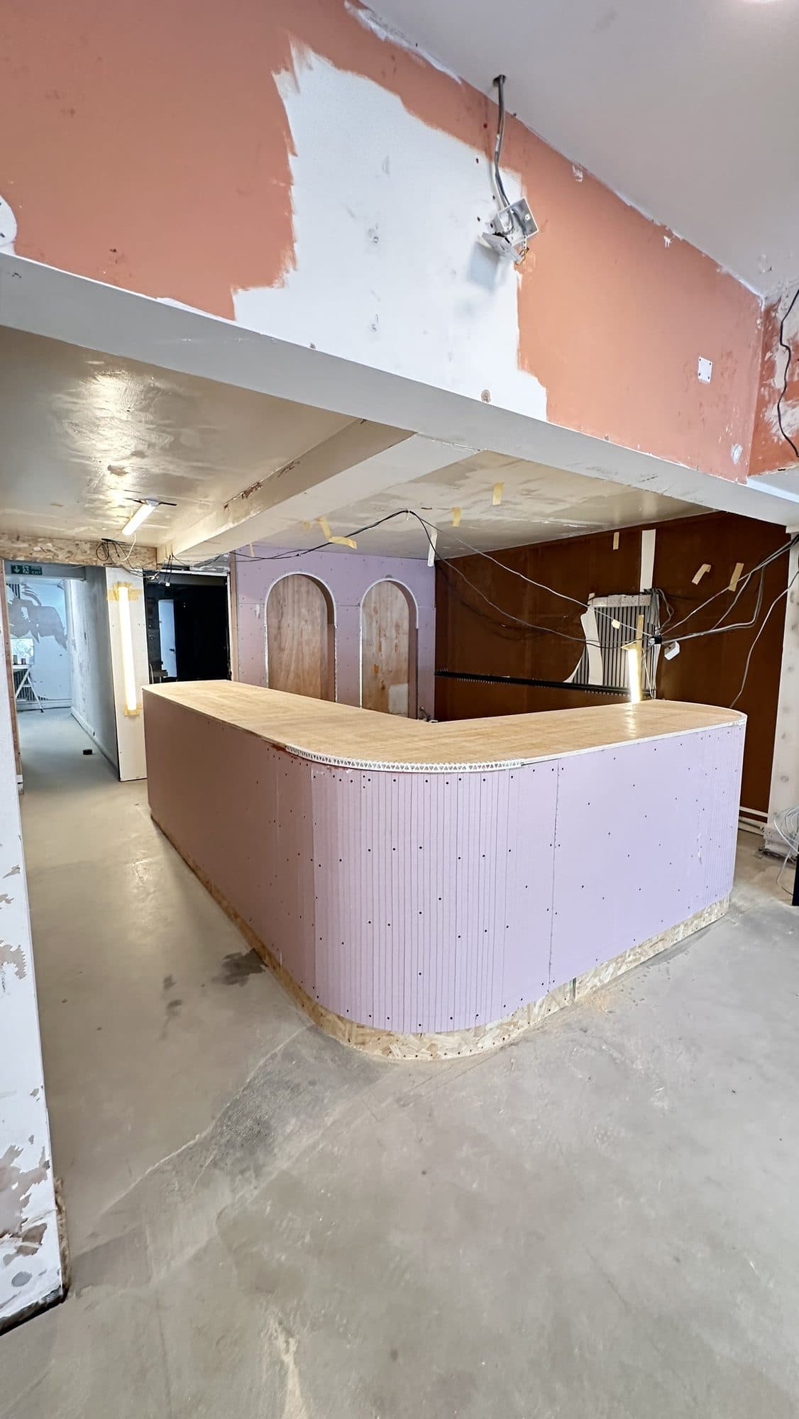Curved reception counter under construction, built up from plywood and OSB with the arched wall recesses visible behind