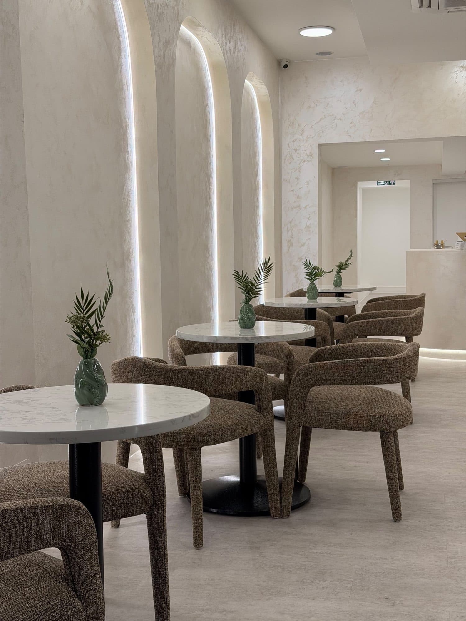 Finished interior view along the seating area toward the reception counter, with illuminated arches and planted café tables
