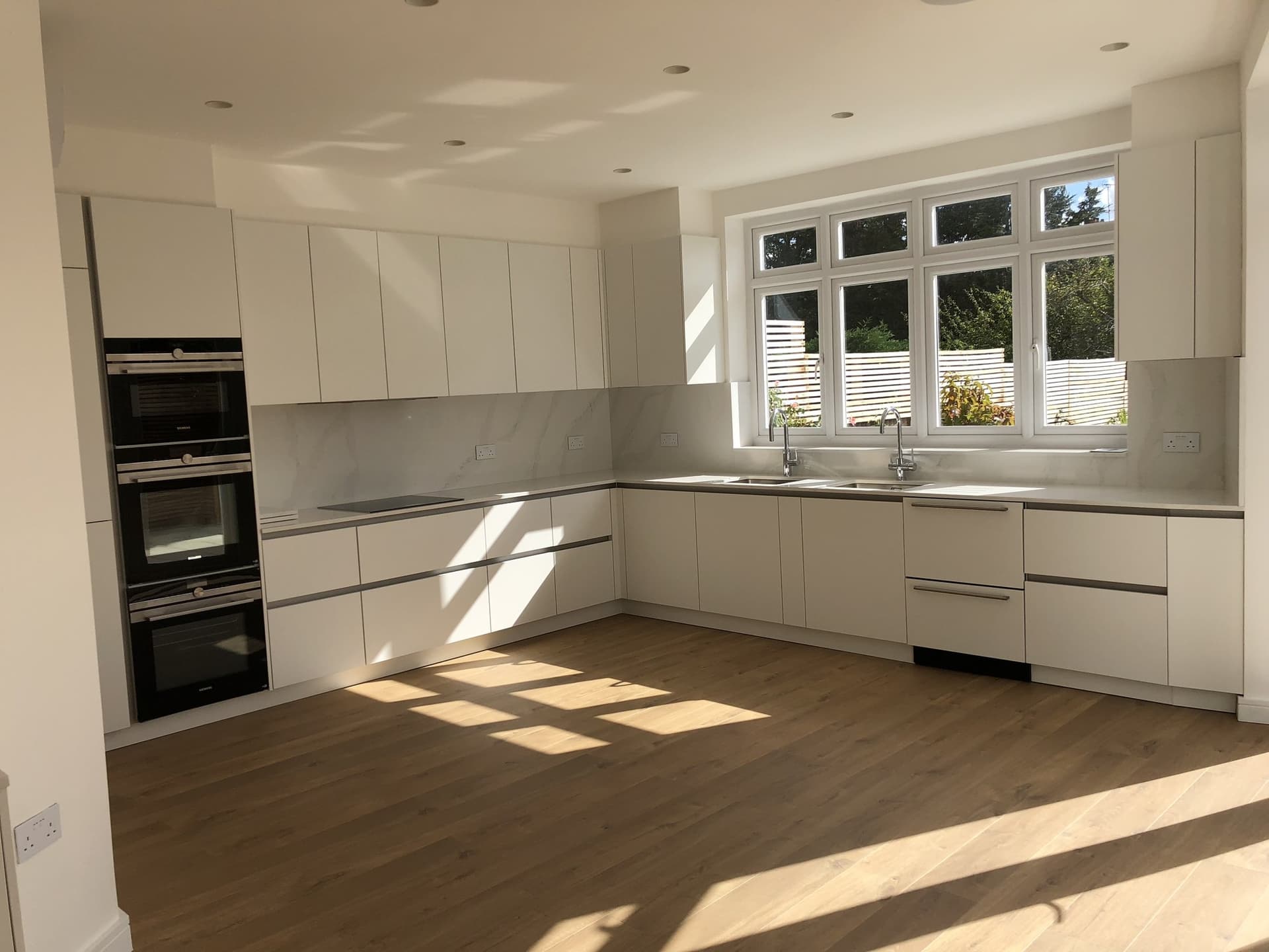 Bright L-shaped kitchen with a marble-effect splashback and a large garden-facing window