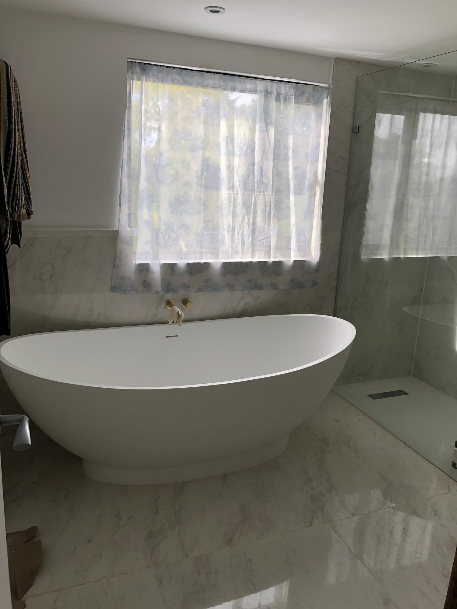 Luxury marble-tiled bathroom with a freestanding oval bath and brass fittings
